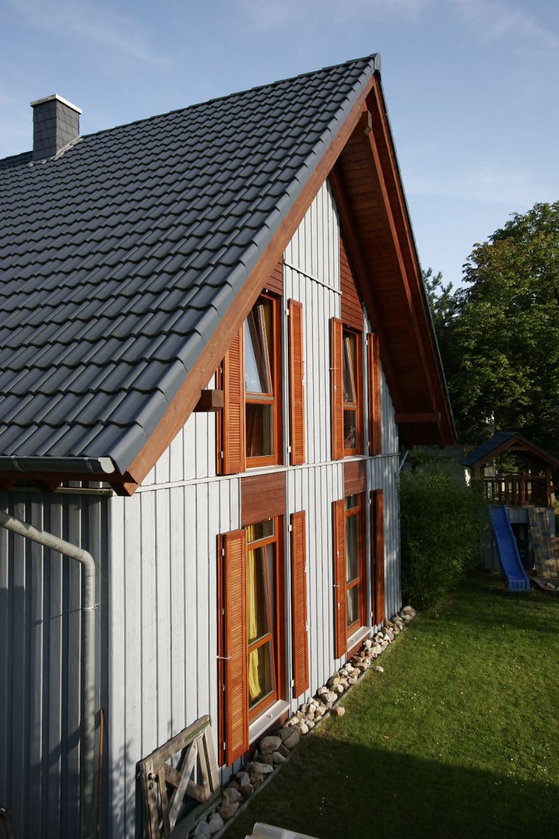 Holzrahmenhaus Seitenansicht mit blauer Verkleidung und Fensterläden
